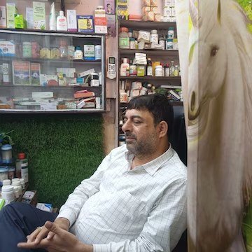 Dr. Asim Zaidi at Shifa Clinic with shelves of Unani medicines behind him